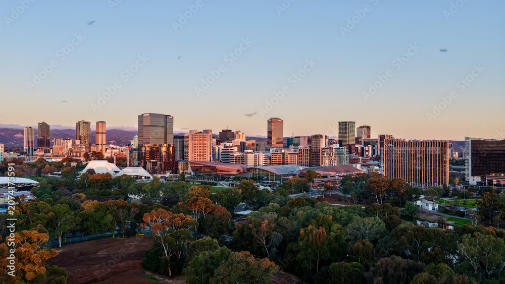 Fototapeta premium Adelaide City, South Australia – 4K aerial drone footage of CBD skyline, Towers, River Torrens, Convention Centre, Elder Park, city bridges and golden sunset cityscape.