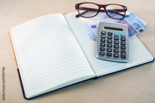 Notebook with blank lined paper, glasses, euro banknotes and a calculator, concept for planning personal finances in a household budget book, copy space, selected focus