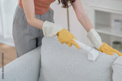 Woman cleaning sofa glove vacuum upholstery living room fabric home hygiene, woman cleaning sofa with handheld vacuum and protective glove bright living room, removing dust from fabric upholstery
