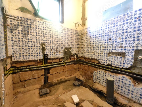 Bathroom renovation and remodeling process. Exposed brick walls, new plastic PPR water pipes, and drain pipes installed during plumbing installation in a messy under-construction room.