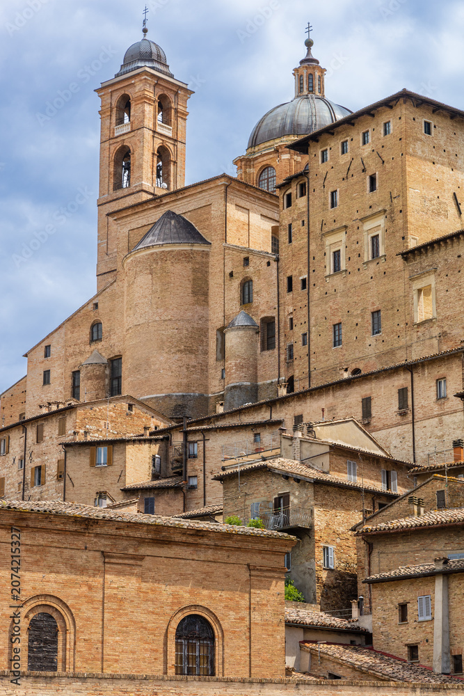 Obraz premium Historic red-brown brick houses of the old town with the Urbino Cathedral (Duomo of Urbino) visible in the distance. Urbino, Marche, Italy.
