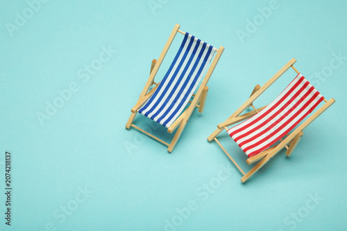 Two miniature deck chairs with red and blue striped canvas seats on blue background. Summer concept.