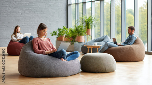 Young gen z people working on laptop in bright workplace with aesthetic bean bag chairs and natural light creating calm vibe