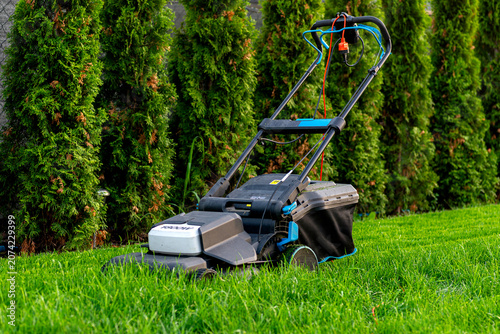Fotografie Electric lawn mower cutting overgrown lawn grass