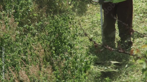 Gardener clearing out almost all overgrown grass and weeds on a plot with a trimmer.