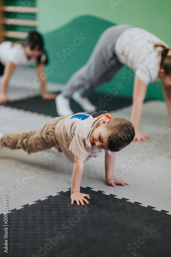 Canvastavla A young boy performs a push-up while other children follow along in a class