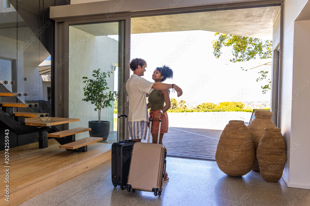 Obraz premium Couple standing near sliding glass door, embracing with wheeled suitcases on terrazzo floor