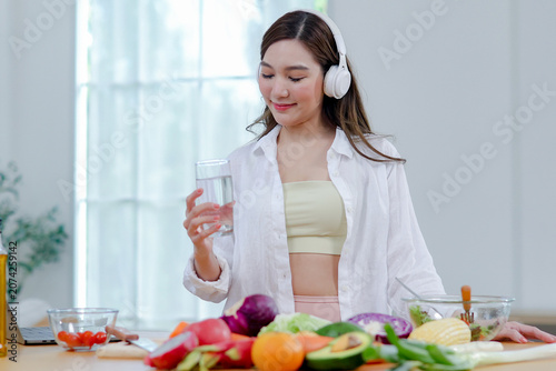 Fotografie Asian women in good spirits hold glass clean water drink while cooking refresh themselves and ensure they have enough water which helps keep their bodies refreshed energetic beneficial health