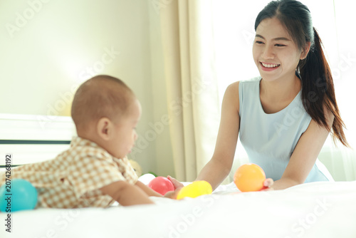 Obraz na płótnie Heartwarming moment love and bonding between mother and her eight month old son in their cozy bed surrounded by brightly colored balls that aid in development provide fun in a joyful atmosphere