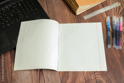 open squared notebook on a wooden table near a laptop keyboard a metal ruler and colored pens