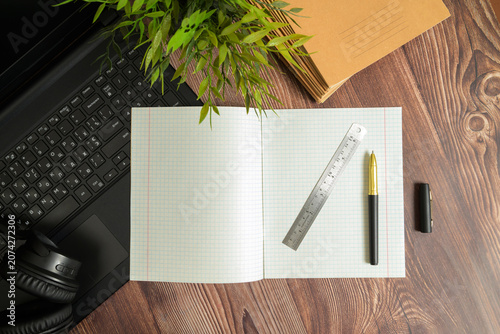 open notebook with a ruler and a pen on a wooden table near a laptop books and a home plant