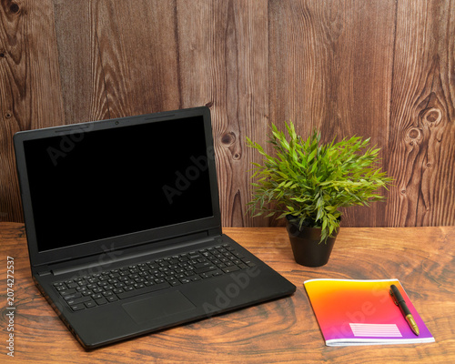 open laptop on a wooden table with a bright notebook