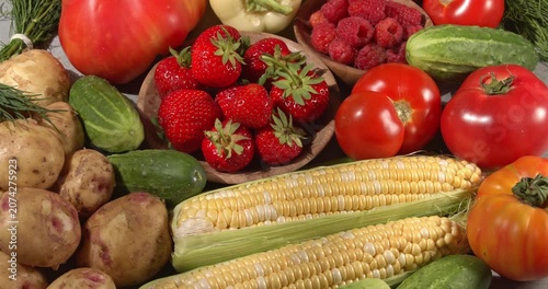 Various fresh healthy products on a gray table. Close-up footage of  corn, strawberries, cucumbers, tomatoes, green onions, potatoes, raspberries, dill, sweet peppers on a rotating table.