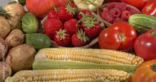 Various fresh healthy products on a gray table. Close-up footage of  corn, strawberries, cucumbers, tomatoes, green onions, potatoes, raspberries, dill, sweet peppers on a rotating table.
