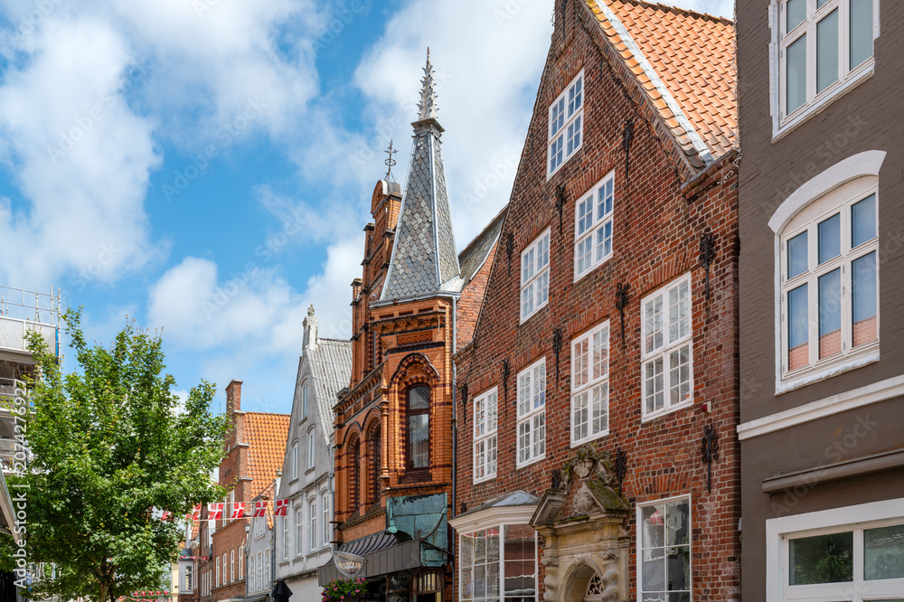 Obraz premium Historic brick houses and richly decorated facades line a picturesque street in the old town of Tønder beneath a blue sky with white clouds.