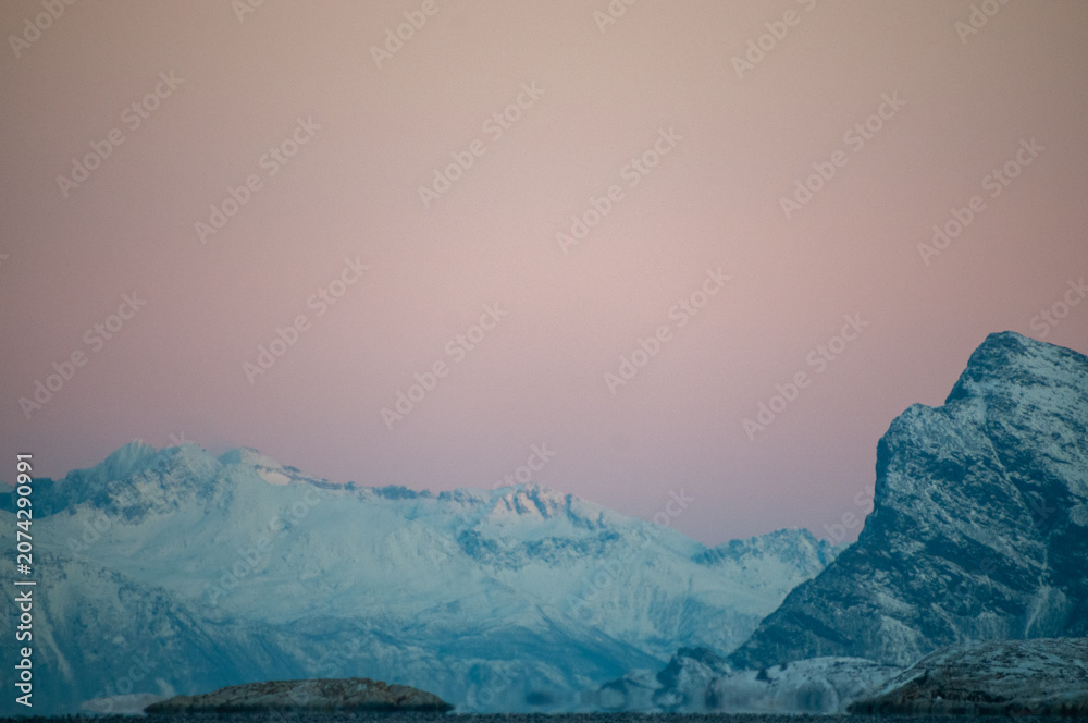 Obraz premium Landscape shot highlighting the rugged mountains and snow-covered beaches of arctic norway during a brief golden hour during the long winters.