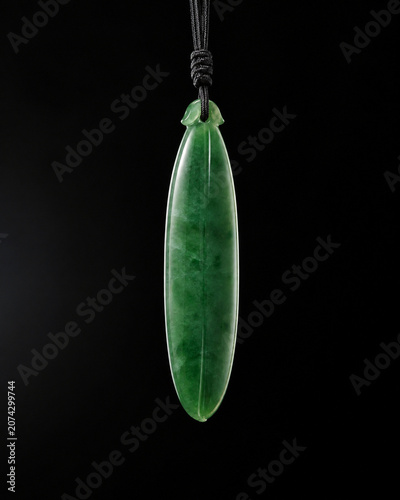 A slender green jade pendant shaped like a silique on a dark background.