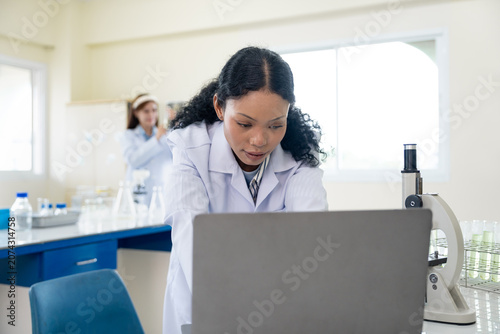 African American female scientist working with microscope and notebook computer in laboratory