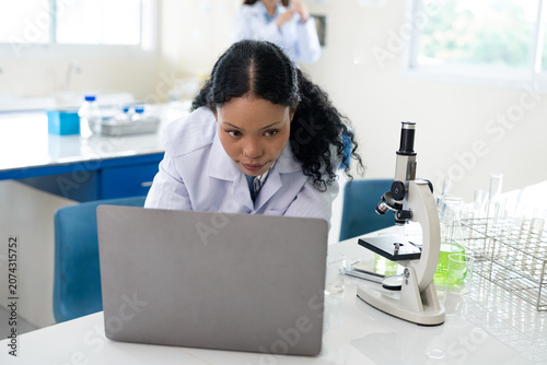 African American female scientist working with microscope and notebook computer in laboratory