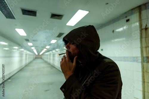 Konstfotografi Hooded man smoking in an empty underground tunnel