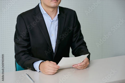 Foto デスクで書類を持ち会議に参加する顔無しの30代の日本人の男性の会社員の顔無しのイメージ
