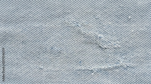 Worn denim fabric with distressed frayed areas and subtle abrasions, close up twill weave showing texture, holes and repairable wear on cotton garment