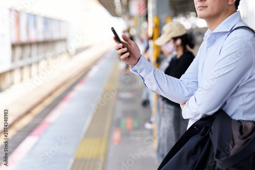 Obraz w ramie 駅のホームでスマートフォンを操作する30代の日本人の男性の会社員の顔無しの匿名イメージ