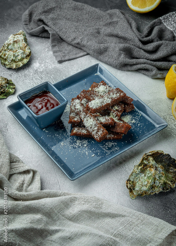 Vertical crispy fried rye bread croutons with grated parmesan and tomato dipping sauce served on a grey textured restaurant table