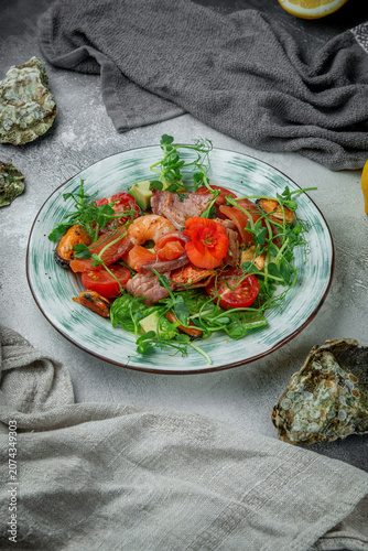 Vertical mixed seafood salad with salmon, shrimp, mussels, avocado, tomatoes, microgreens and edible flower on a grey restaurant table