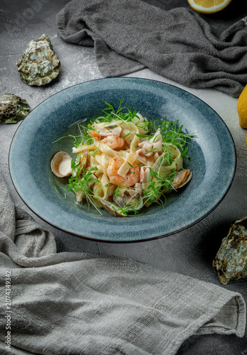 Vertical seafood tagliatelle pasta with shrimp, clams, fresh microgreens and light creamy sauce served in a blue restaurant plate