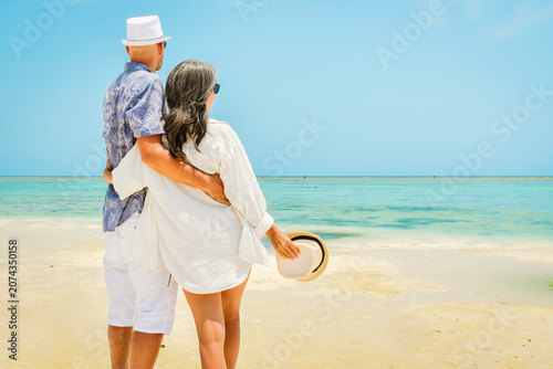 Canvas-taulu Couple stand together hugging hug enjoy arms up on white sand beach in sunny tropical destination