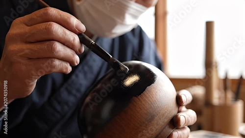 A craftsman applies a protective lacquer finish to a traditional Japanese wooden bowl, highlighting meticulous artistry