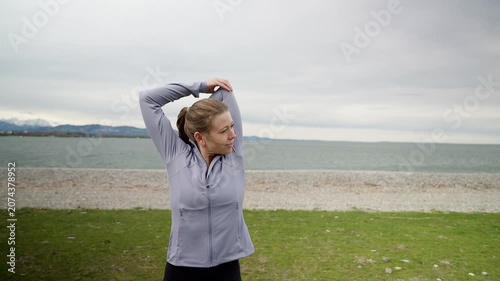 Active woman stretching arms before running by the sea
