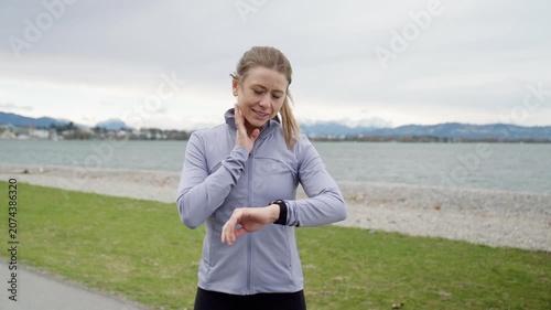 Sporty woman checking pulse and smartwatch after running outdoors