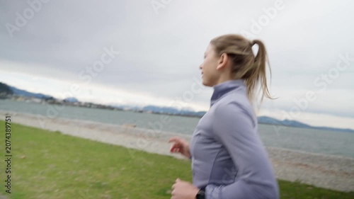 Determined young athletic woman running along the lake shore