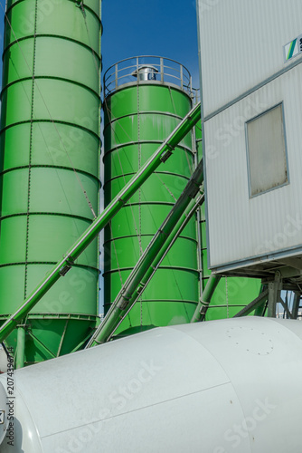 Green industrial silos and storage tanks at a concrete batching plant under a clear blue sky, modern eco-friendly construction industry and manufacturing infrastructure