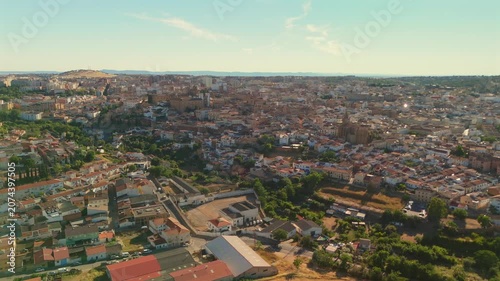 Drone flies backward from the historic center of Caceres, gradually revealing the full extent of the city surrounded by green Extremadura landscape.