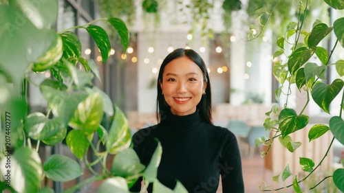 Young woman in black turtleneck standing centered between lush hanging indoor vines and foliage, soft bokeh lighting, office or cafe atmosphere.