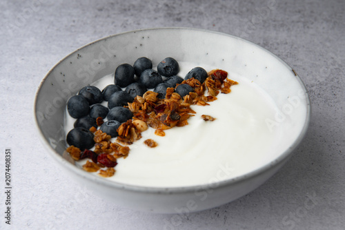 Yogurt bowl with granola and fresh blueberries on a light stone background