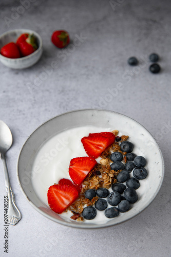Healthy yogurt bowl with granola, blueberries, and strawberries on a light table