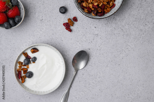Flat lay of a yogurt bowl with granola and berries on a light textured background