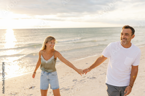 Couple holding hands walking beach at sunset