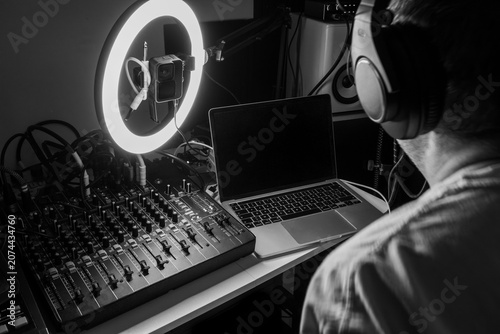 Music producer working in a home recording studio with audio mixing console, laptop, and ring light, classic monochrome edit.