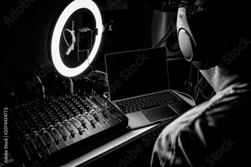 Music producer working in a home recording studio with audio mixing console, laptop, and ring light, presented in a high-contrast black and white style.