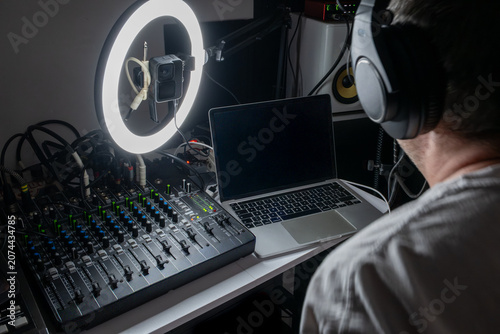 Music producer working in a home recording studio with audio mixing console, laptop, and ring light, natural interior lighting setup.