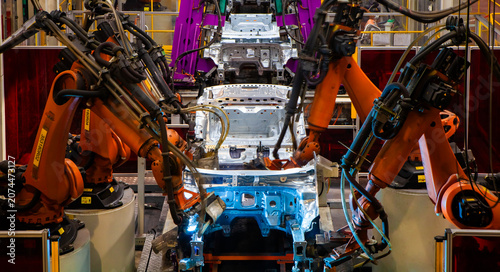 Foto Robotic arms at an auto factory are welding car bodies.