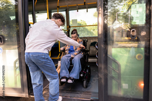 Young man assisting woman in wheelchair entering public bus