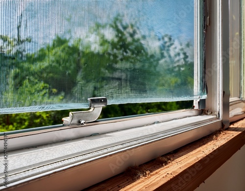 window frame with an insect screen focusing on the seal hinge and dirty sill representing home repair and durability