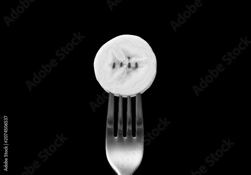 A single slice of ripe banana impaled on the tines of a silver fork, presented against a stark transparent background, isolated on transparent background