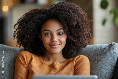 Beautiful young woman with curly hair sitting on a sofa at home using a laptop computer